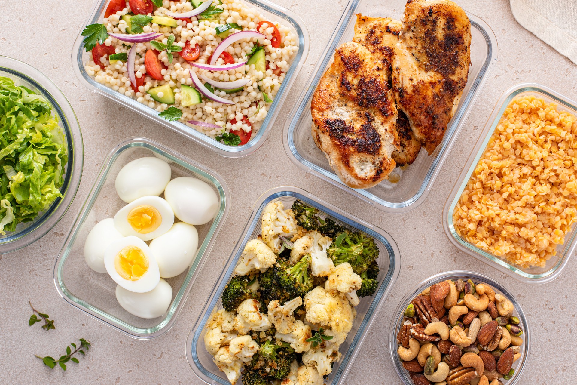 Healthy meal prep with cooked chicken breast, boiled eggs, roasted vegetables, cooked lentils, couscous salad and nuts