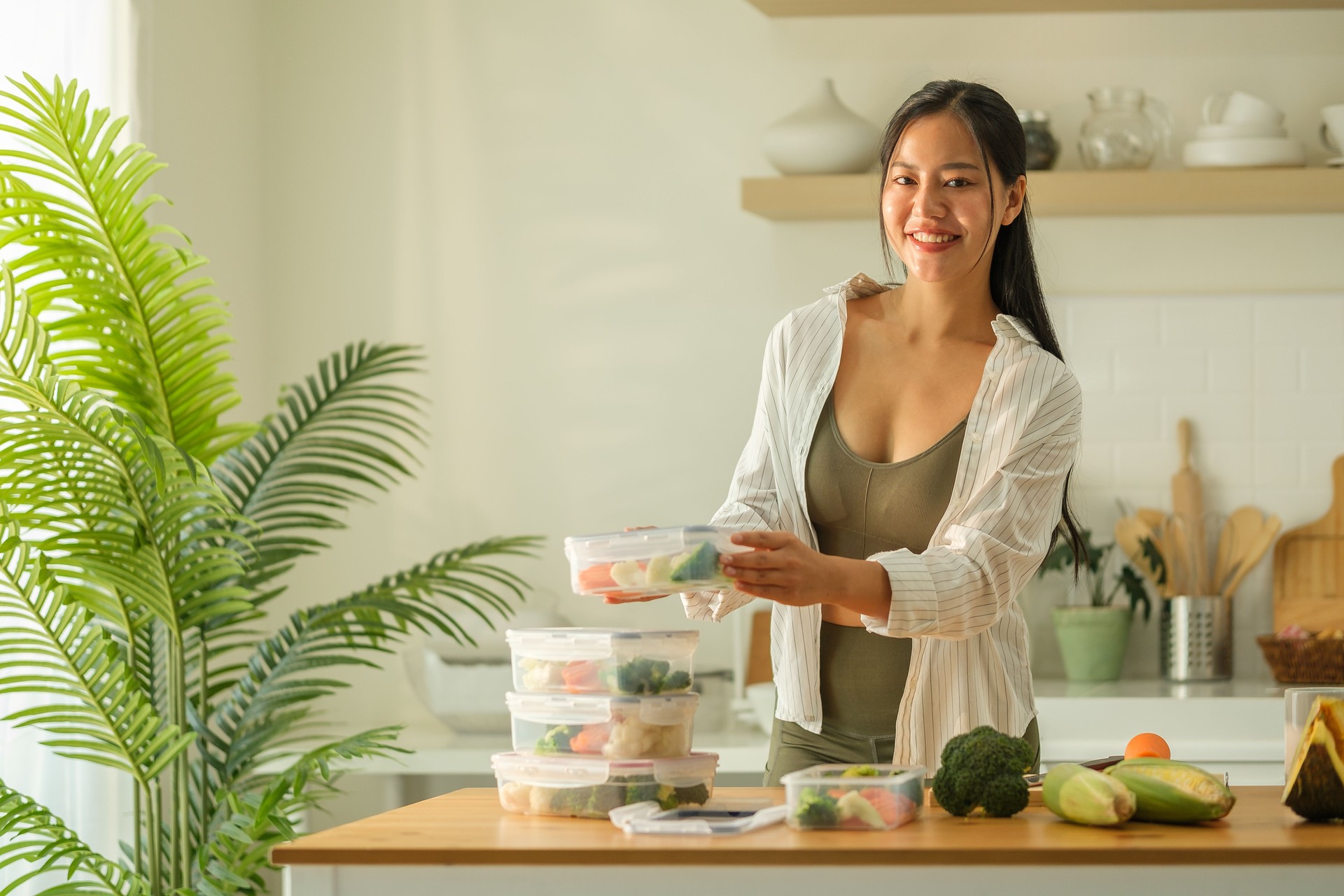 Attractive woman arranging her meal prep containers on the kitchen counter, ready for a week of healthy eating. Healthy lifestyle and nutrition concept.